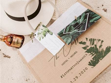 A beach scene with a white hat, sunglasses, a bottle of liquor, a sandals note, a knocked-open package, and a postcard on sand.