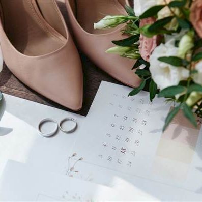 A wedding scene: blush heels, a bouquet with pink and white roses, rings, and a calendar spread on a table with soft light.