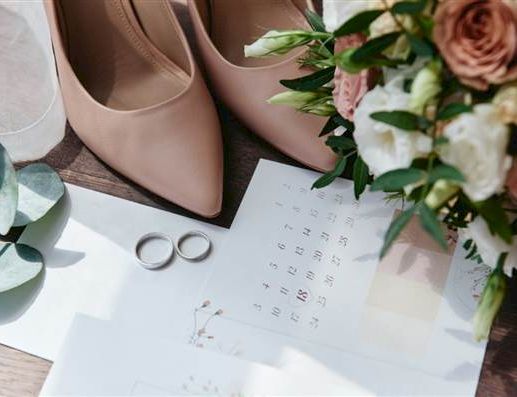 A wedding scene: blush heels, a bouquet with pink and white roses, rings, and a calendar spread on a table with soft light.