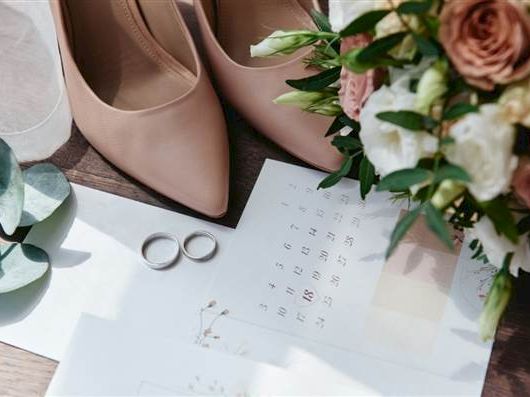 Elegant wedding setup with blush heels, a bouquet, rings, and a calendar&mdash;hinting at a special date and vows.