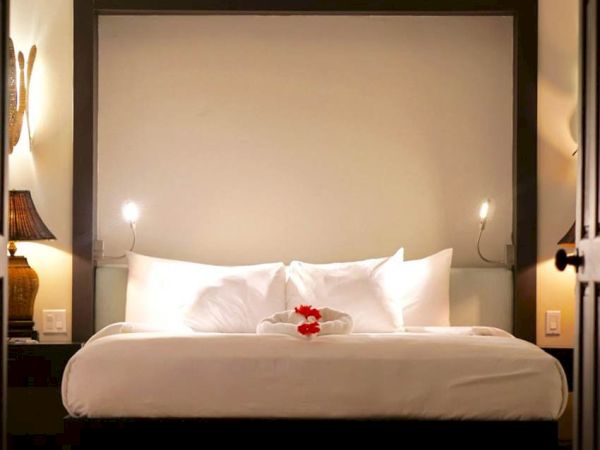 A luxurious hotel room with a large neatly made bed, white linens, two lamps, and a flower on the pillows, cozy and elegant.