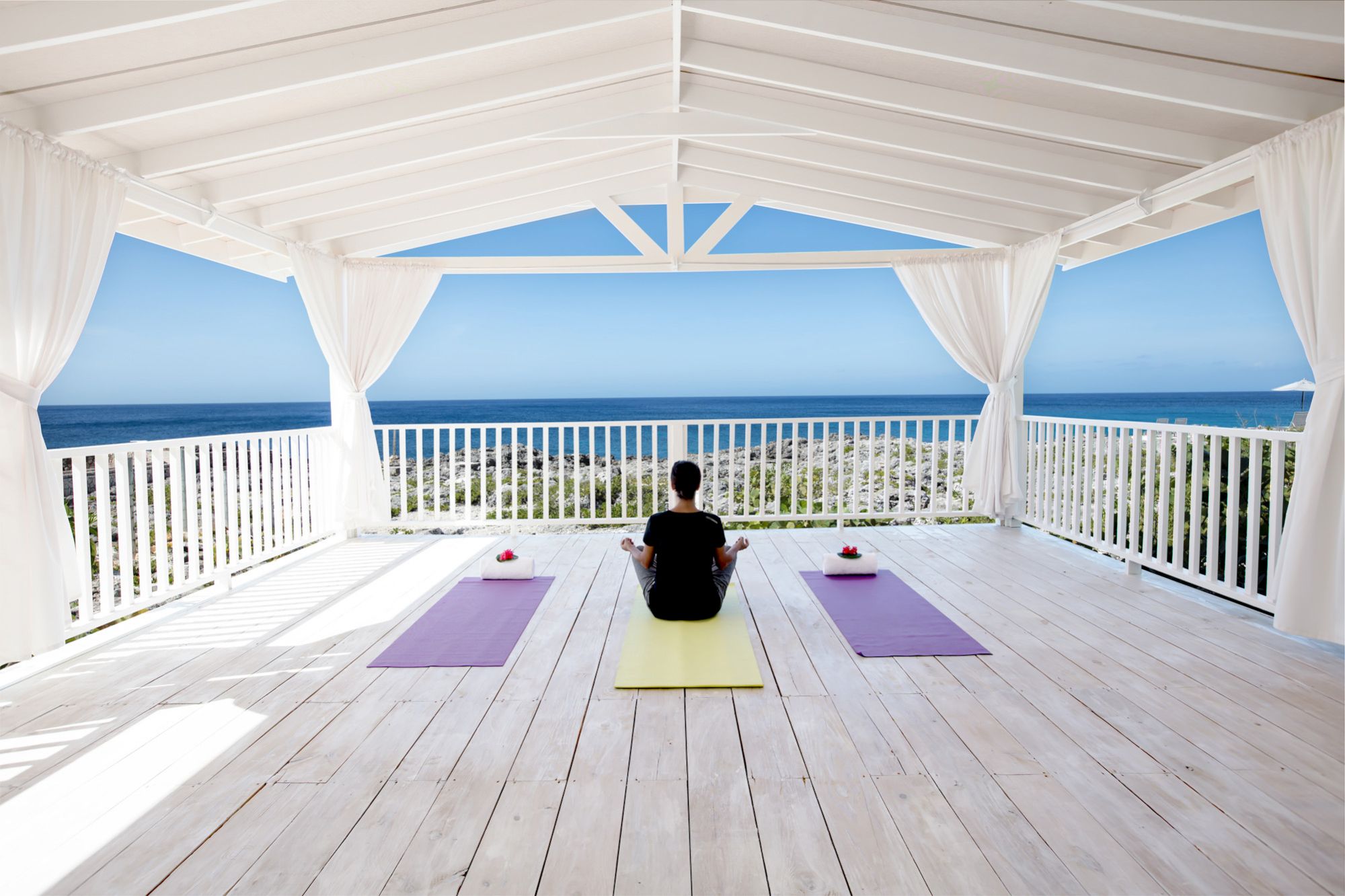 A peaceful oceanfront yoga session on a white deck with three mats facing the sea, under a bright, airy shelter.