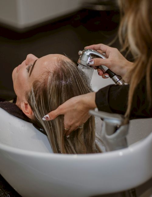 A person is getting a hair wash at a salon, with a stylist rinsing their hair over a sink.