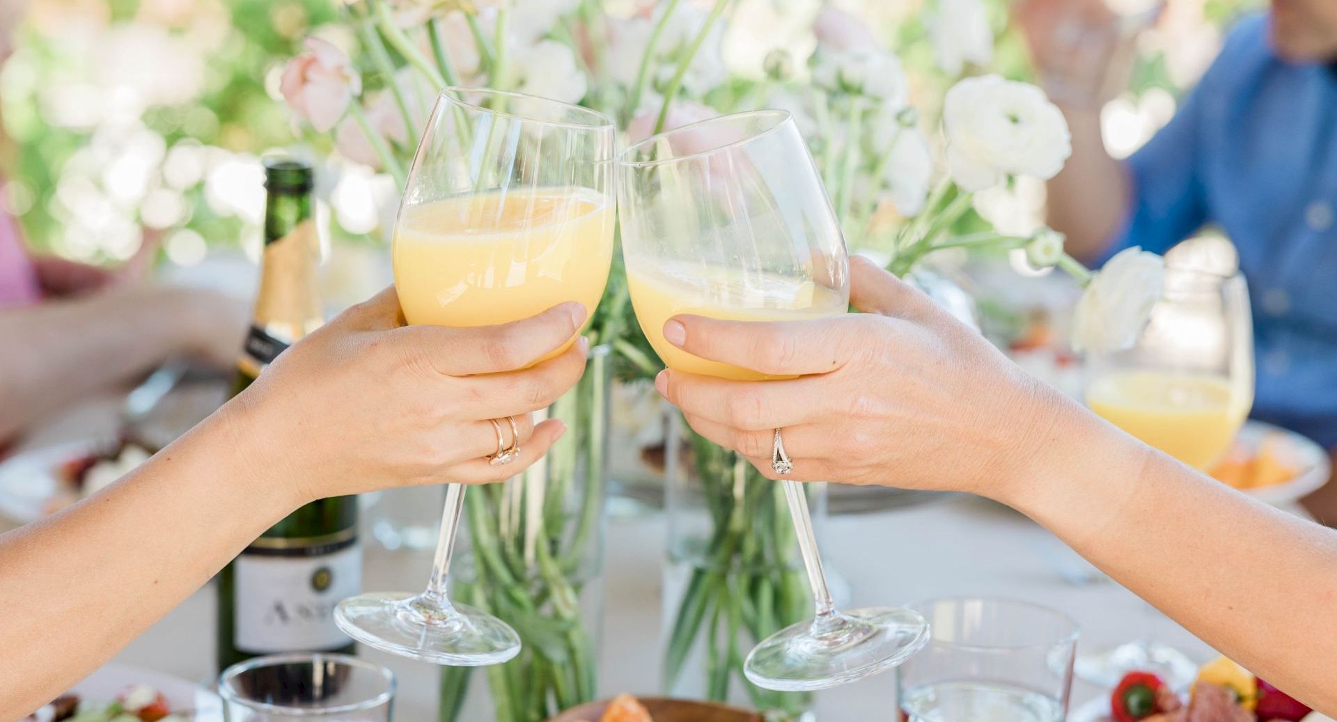 People clinking wine glasses in a cheerful toast at a table with flowers and drinks.