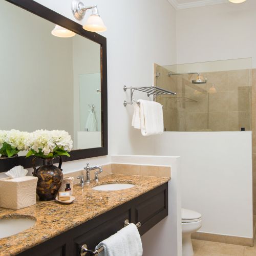 Amodern bathroom with a double vanity, granite countertops, large mirror, and a glass-enclosed shower; towels and flowers add a decorative touch.