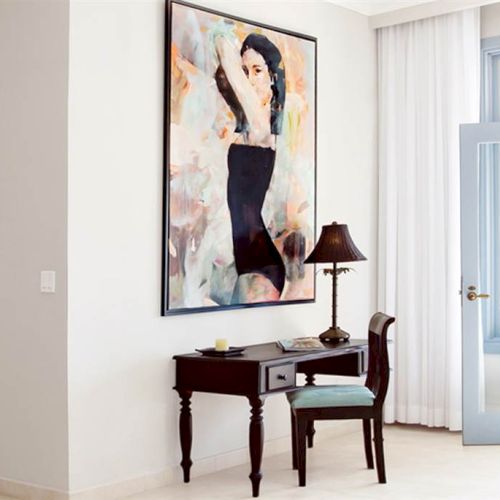 A modern white-walled room with a black desk, chair, a large portrait, and a glass door leading to another space.