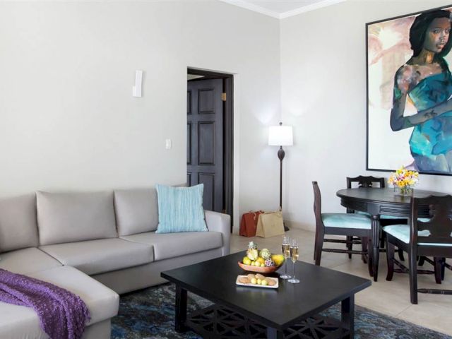 A modern living room with a gray sectional, teal throw pillows, and a purple blanket; a black coffee table, dining set, and a large wall art of a woman.