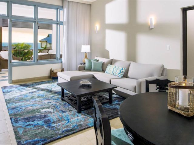A bright, modern living room with a gray sofa, turquoise accents, a blue patterned rug, and a view of a balcony through large windows.