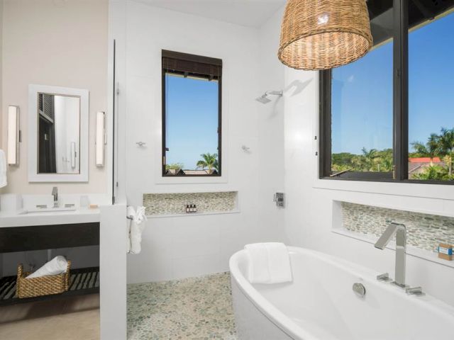 A modern white bathroom with a freestanding tub, mosaic tile floor, large windows, and a woven pendant light, offering bright natural light.