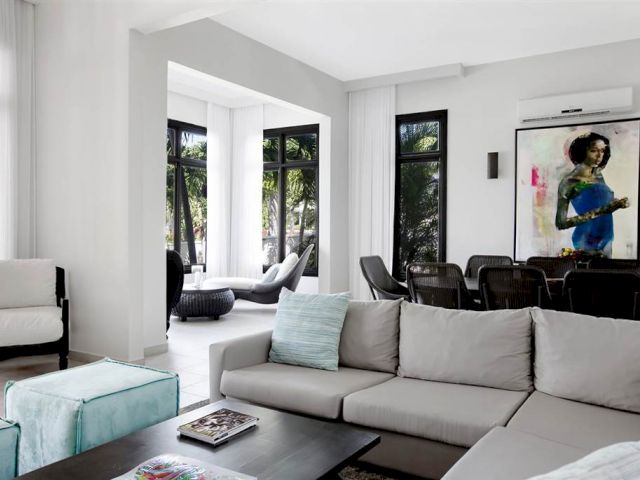 A bright, modern living room with a large gray sectional sofa, black chairs, a coffee table, and a vibrant wall painting; plenty of natural light.