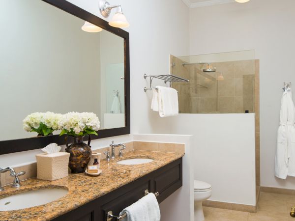 A modern bathroom with a double sink vanity, granite countertops, a large mirror, towel rack, and a separate tiled shower area with a glass door, all in neutral tones.