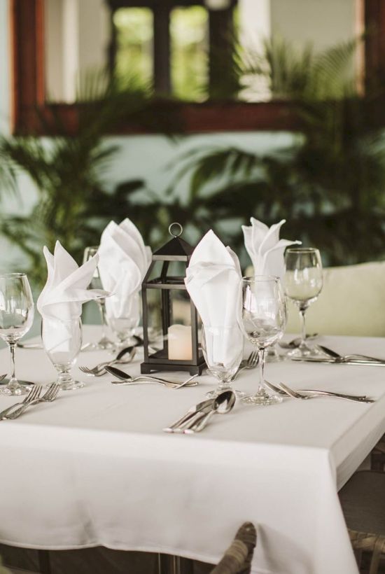 Elegant table setting with folded napkins, wine glasses, and a decorative lantern centerpiece in a softly lit dining area.
