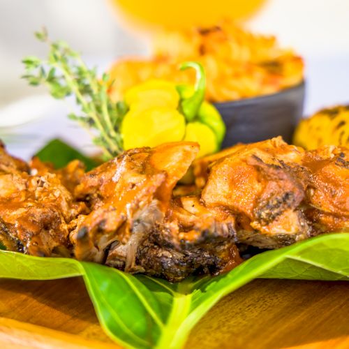 Grilled meat on a green leaf with herbs and sunflower garnish, plated as a dish with a vibrant, tropical presentation.