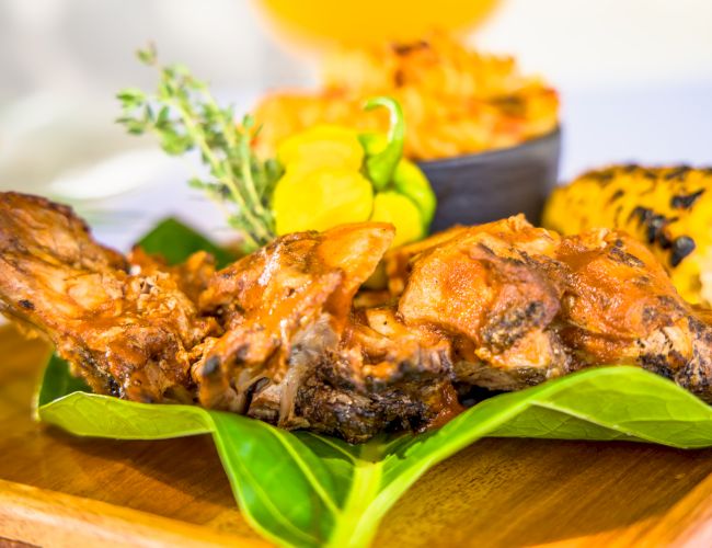 Grilled meat on a green leaf with herbs and sunflower garnish, plated as a dish with a vibrant, tropical presentation.