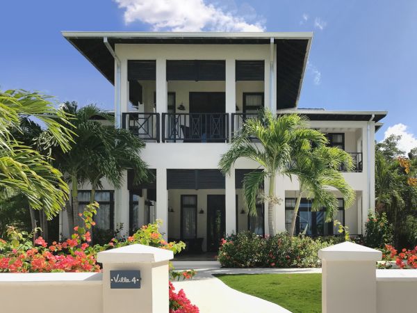 A modern two-story house with white walls, dark trim, a covered balcony on the second floor, and tropical landscaping including palm trees.