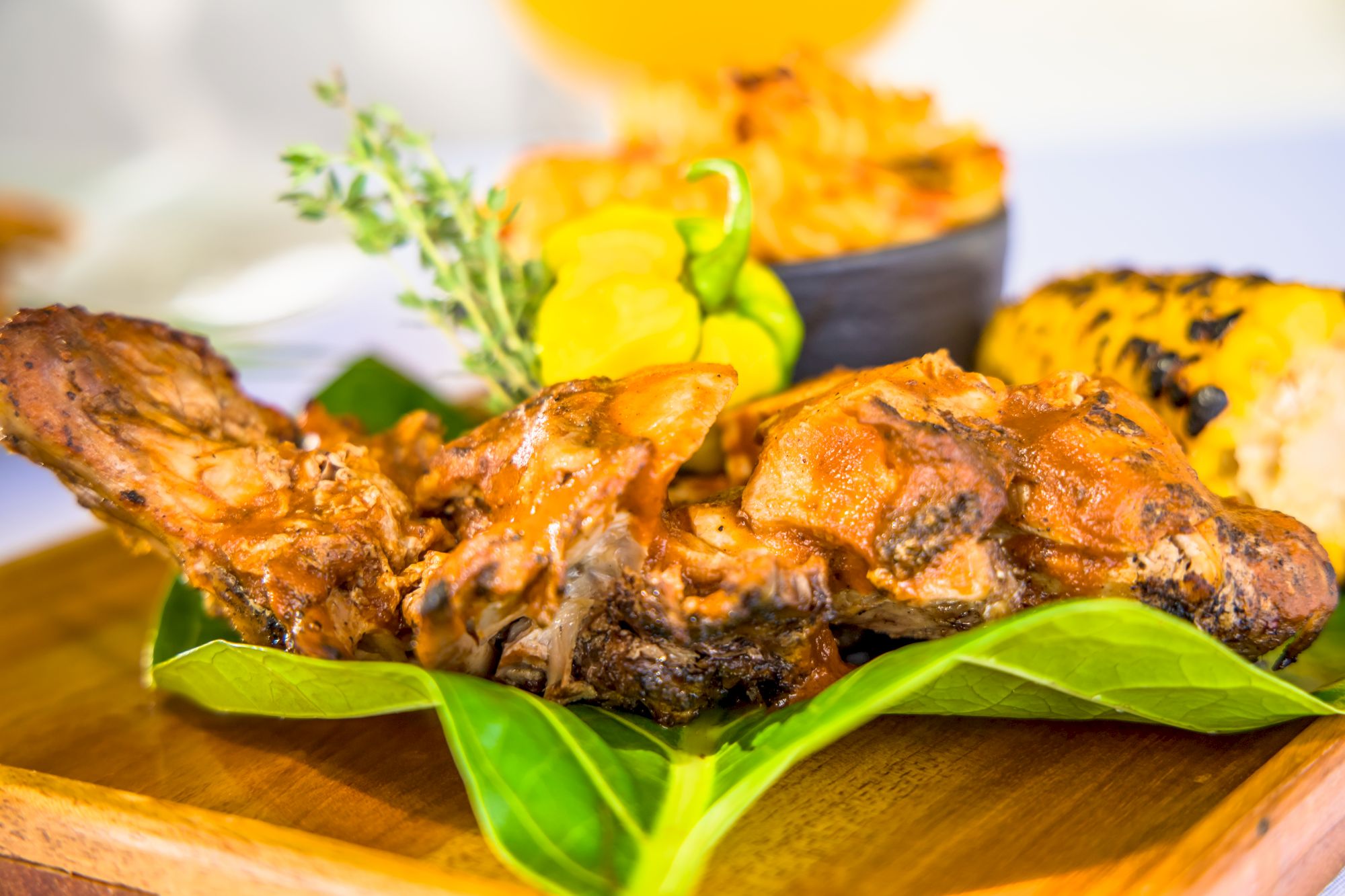 Succulent grilled meat served on a leaf, garnish with lemon and herbs, plated on a wooden board with a bright, colorful background.