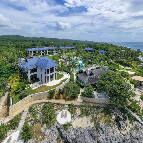 A coastal cliffside village with winding paths, turquoise sea, and rugged rocks under a bright blue sky.