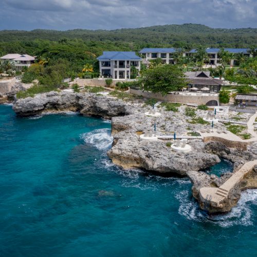 A stunning rocky coastline with turquoise water, clear skies, and a charming seaside village nestled along the shore.