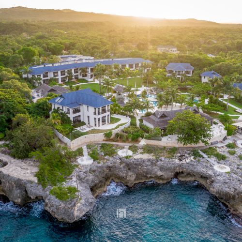 A coastal town perched on cliffs overlooks turquoise water and a rocky shoreline at sunset.
