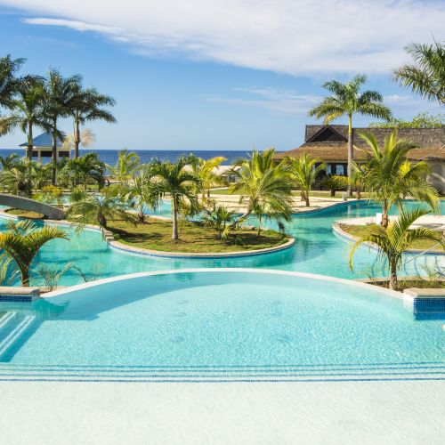 A bright resort pool scene with clear blue water, loungers, palm trees, and sunshine by a sunny hotel.