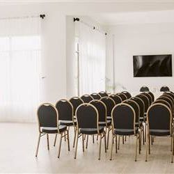 A bright, minimalist conference room set with rows of black and gold chairs facing a wall-mounted screen, ready for a presentation.
