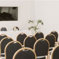 A small conference room with rows of black cushioned chairs, a long table at the front, and a flat-screen monitor on the wall.