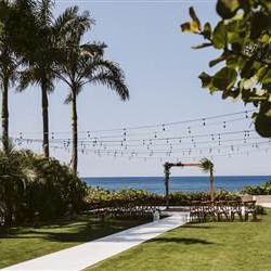 A lakeside scene with a wooden pier, trees lining the shore, calm water, and a clear sky reflecting sunlight, ending with a period.