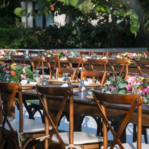 A sunny outdoor caf&eacute; scene with wooden tables and chairs, people dining under trees by a street&mdash;pleasant, bustling, and relaxed.