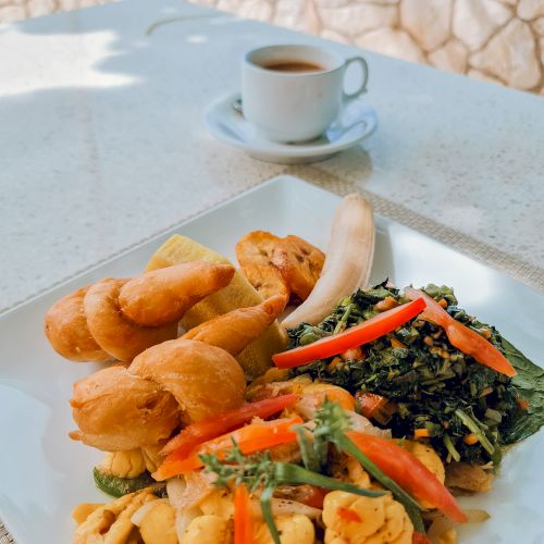 Delicious plate with croissants, saut&eacute;ed vegetables, greens, and chicken, plus a cup of coffee in the background, on a sunny outdoor table.