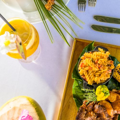 A vibrant brunch: fried shrimp skewers, fresh greens, bright orange mango salsa, a grilled meat dish on a wooden plate, citrus drinks, and a pastel table setup.