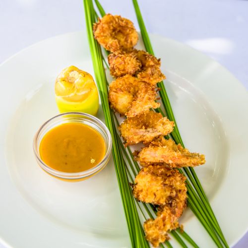 Crispy fried shrimp skewers with dipping sauce and a dollop of mustard, arranged on green onions on a plate.