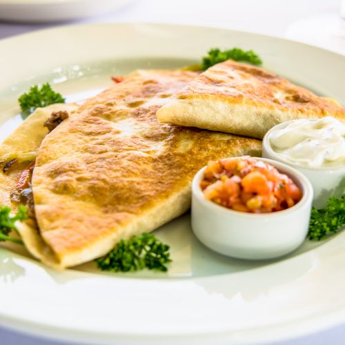 A plate with two quesadillas, a dollop of sour cream, a small salsa cup, and leafy greens garnish. Ending with a period.