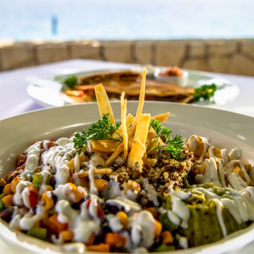 A colorful plate of assorted sushi and toppings with crispy sticks and greens, set against a seaside background, delicious and vibrant.