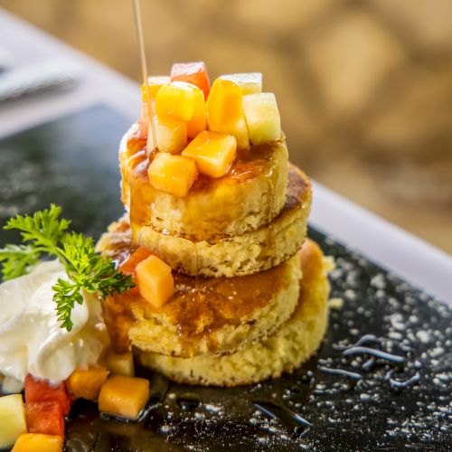 A stack of golden crumbed fried rounds topped with diced mango/papaya cubes, a dollop of cream, and a sprig of herbs, drizzled with syrup.