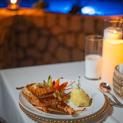 A romantic dinner setup with a lobster dish, mashed potatoes, candlelight, and wine glasses on a white tablecloth, soft evening ambiance.