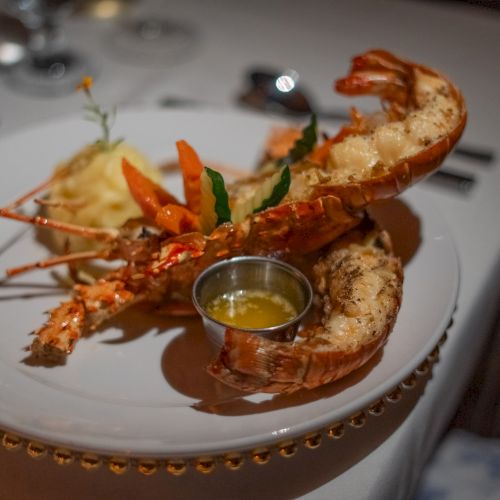 A plate with two large grilled lobsters tails and a small cup of melted butter or sauce, served on a fancy white dish at a restaurant.