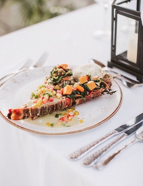A gourmet plate with a sliced beef tenderloin topped with colorful vegetables and sauce, elegant table setting with a lantern in the background.